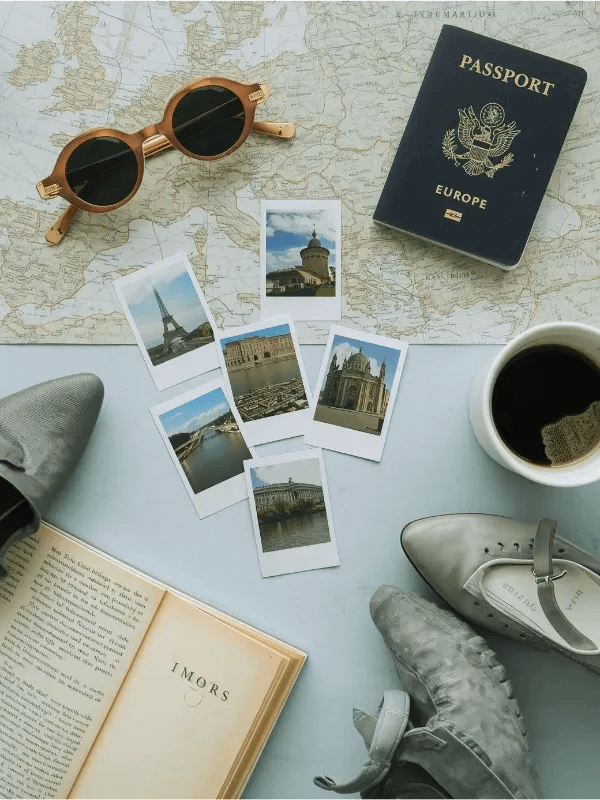 Vertical photo (800x1200) showing a moodboard-style flat lay with Europe travel inspiration_ map, passport, sunglasses, polaroid photos, cute shoes, travel guidebook, and a coffee cup. Light blue tones, modern, fe
